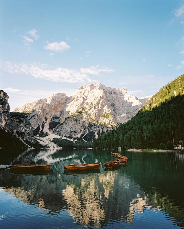 Wooden boats float on a lake with mountains and a forest in the background.