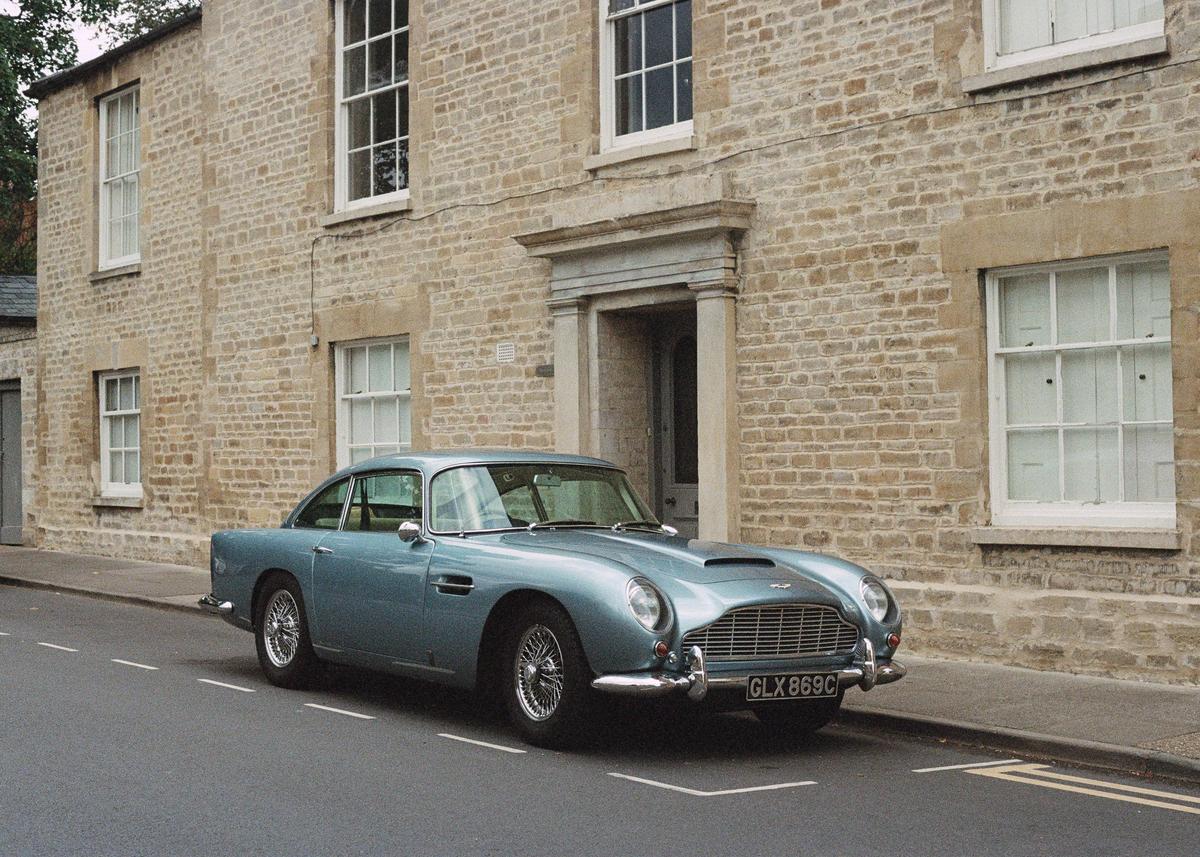 A blue vintage car is parked on a street in front of a stone building with white windows.