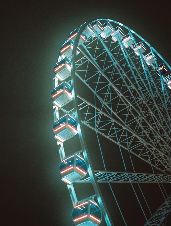 A ferris wheel with illuminated gondolas is visible against a dark night sky.
