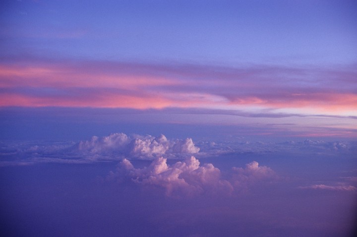 Clouds are visible from above with a purple and pink sky.