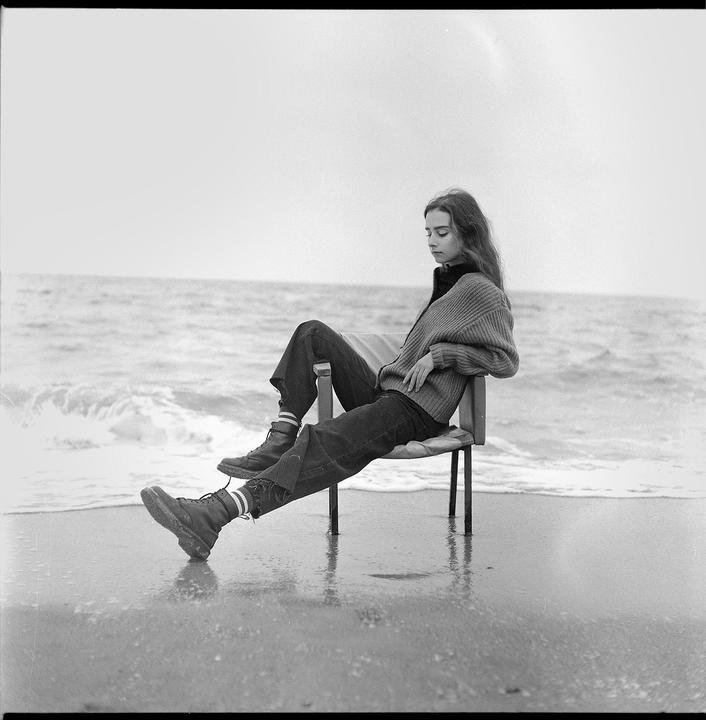 A woman sits on a chair in the shallow water at the edge of the ocean.