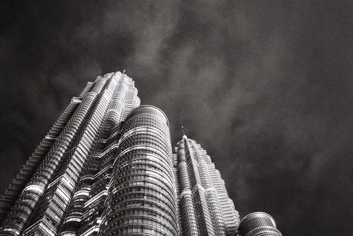Two tall, modern buildings with intricate designs reach towards a cloudy sky.