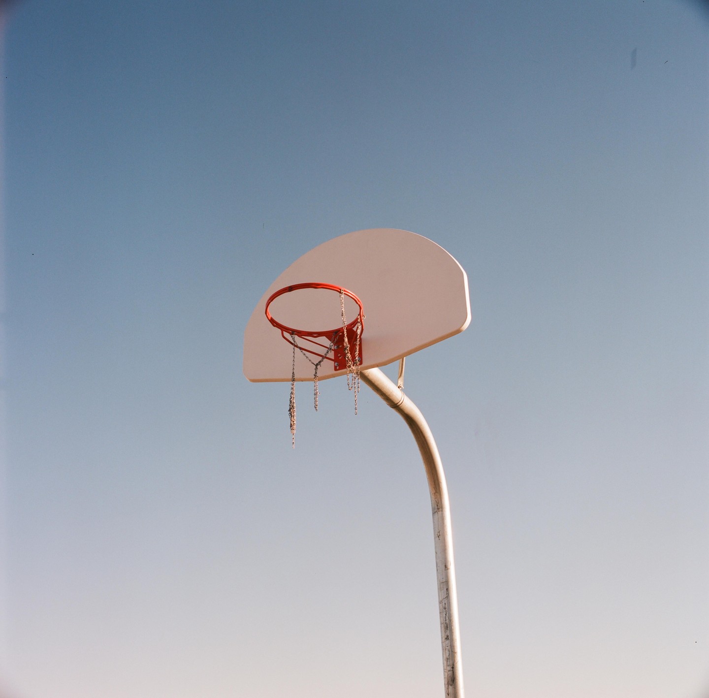 A basketball hoop with a chain net stands against a clear blue sky.