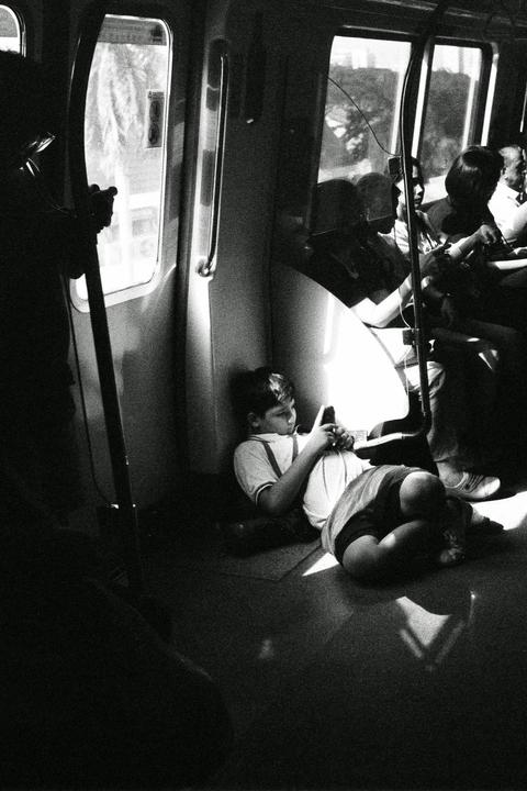 A boy sits on the floor of a train car, looking at his phone.