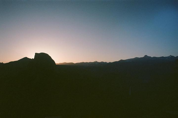 The sun rises behind a mountain range, silhouetting the peaks against a gradient sky.