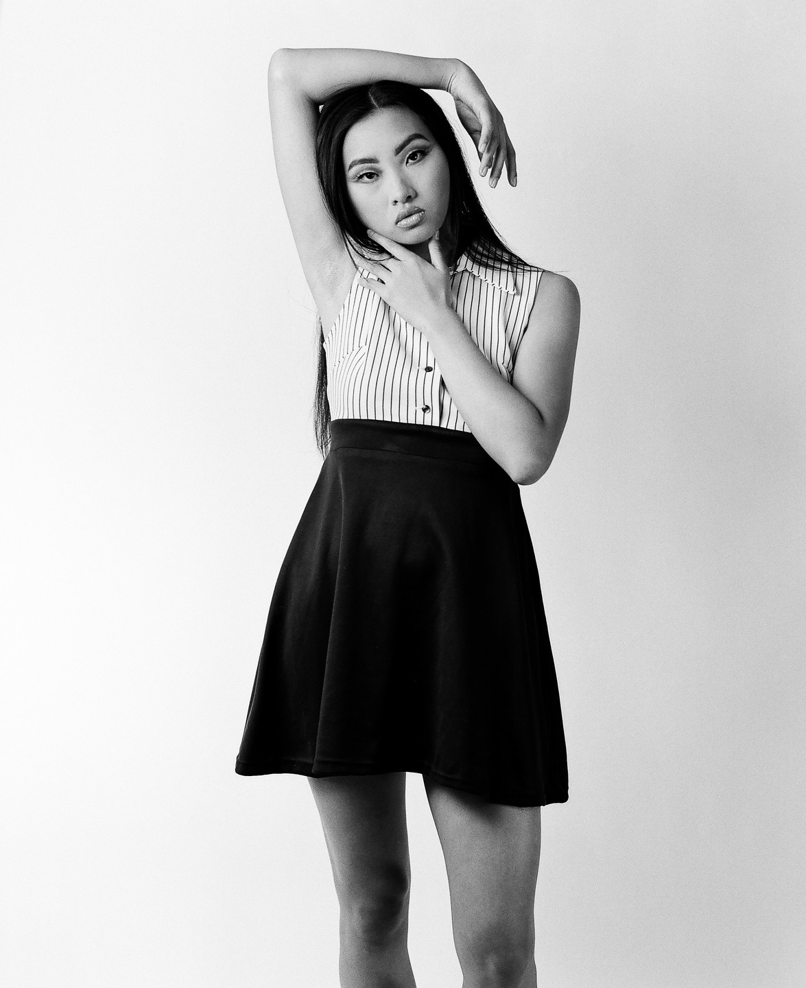 A woman in a striped top and dark skirt poses with her arms raised above her head.