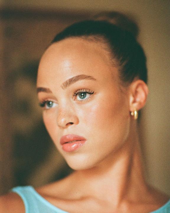 A woman with her hair in a bun and wearing a light blue top looks to the side.