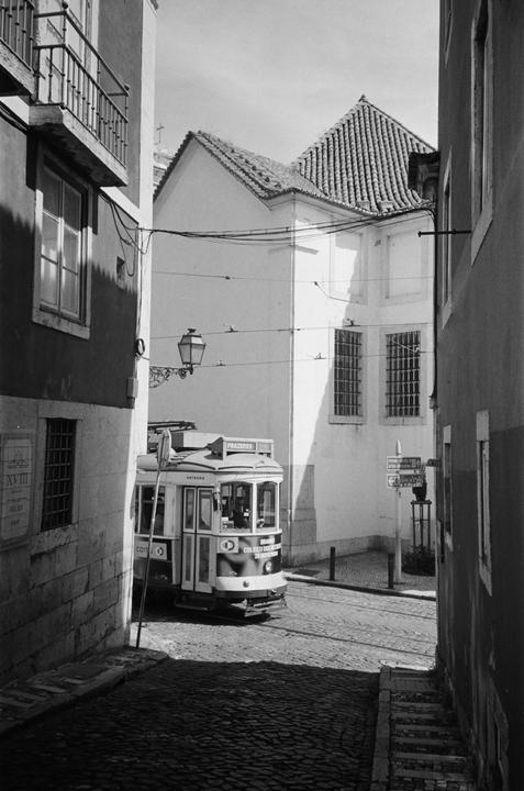 A tram is visible on a cobblestone street in a narrow alley in Lisbon.