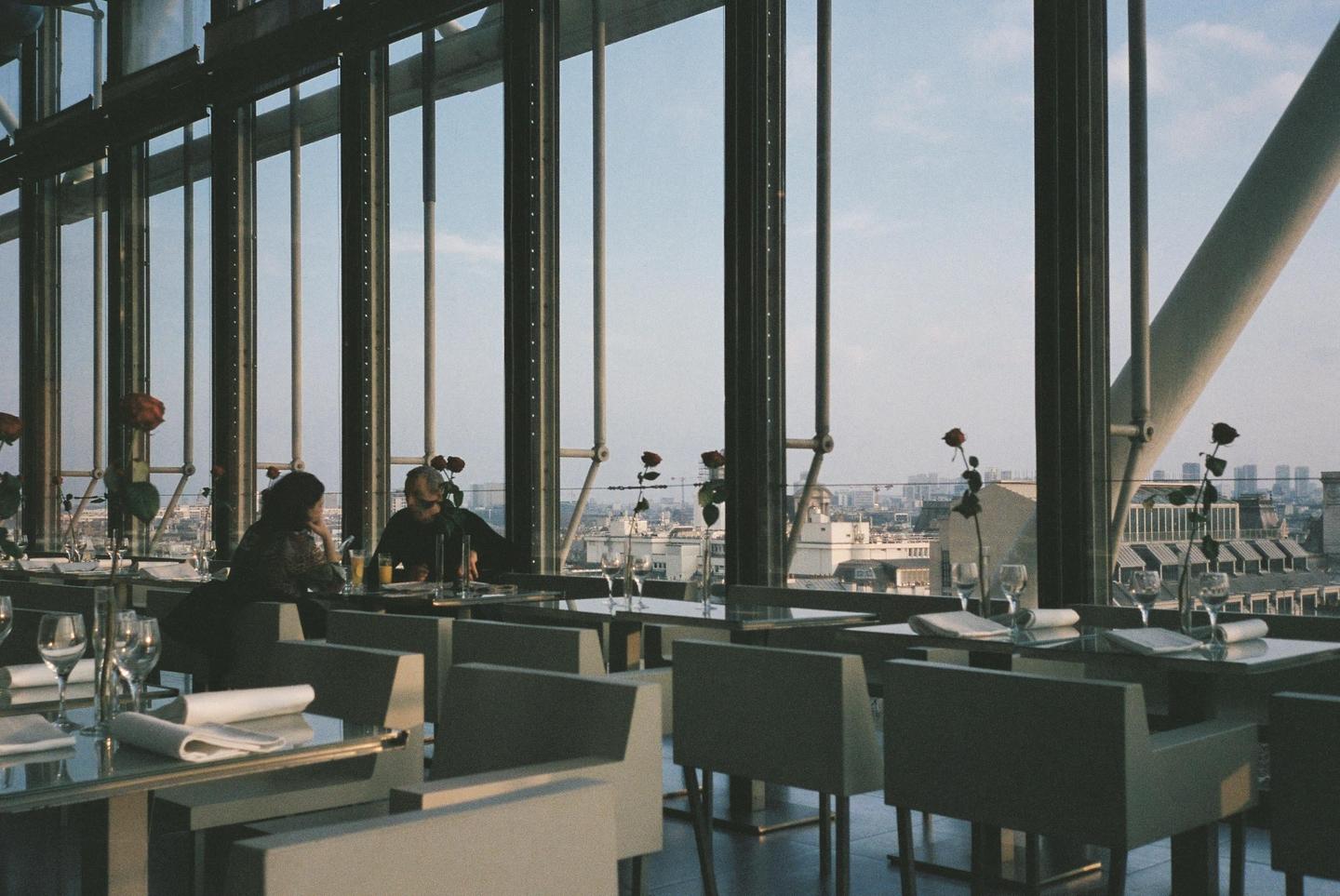 A couple sits at a table in a restaurant with large windows overlooking a city.