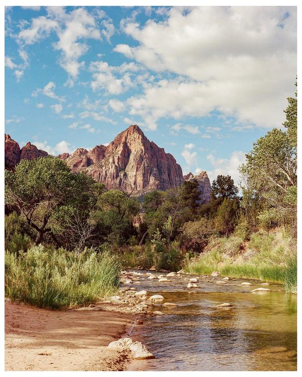 A river flows through a valley with mountains and trees under a cloudy sky.