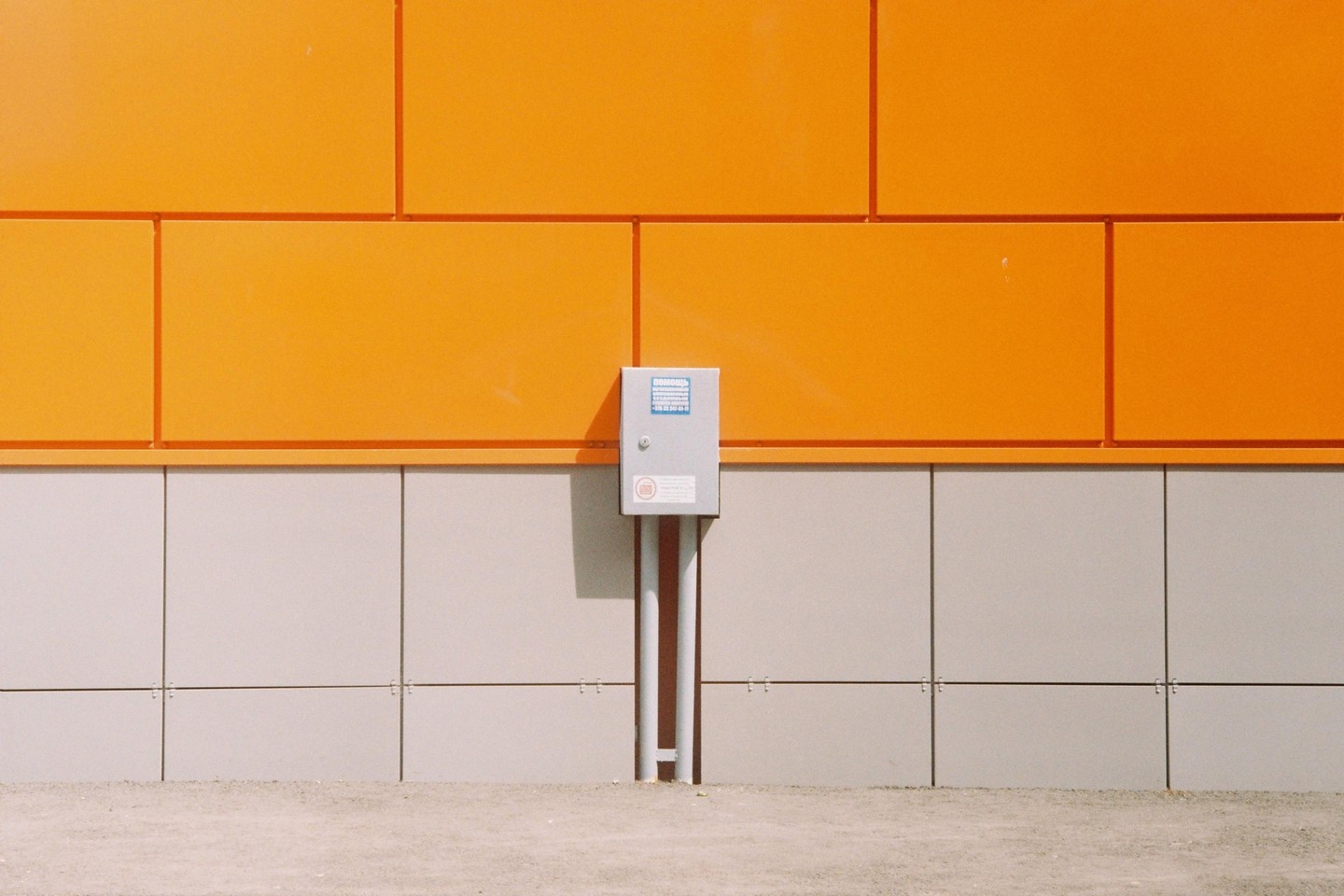 A gray electrical box is mounted on a wall with orange panels on top and gray panels on the bottom.
