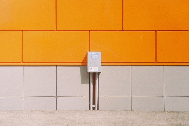 A gray electrical box is mounted on a wall with orange panels on top and gray panels on the bottom.