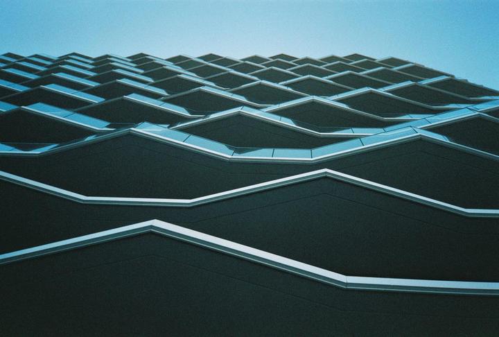 A modern building with a wavy facade and balconies is photographed from below against a clear sky.