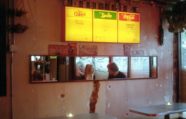 A couple sits at a table in a diner with menu boards and license plates on the wall.