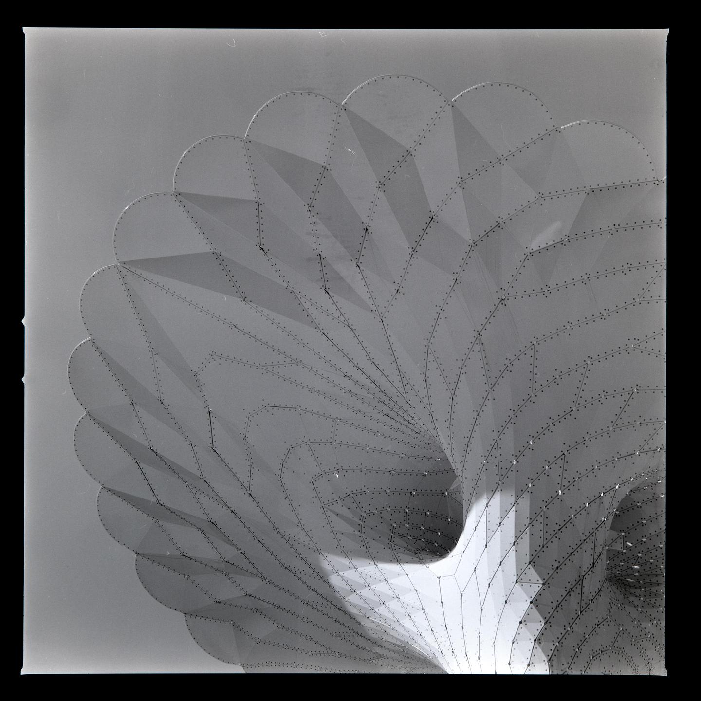 A large, curved, perforated metal structure with a scalloped edge is shown from below.