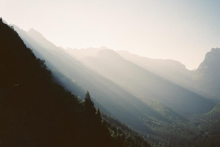 Sunlight streams through a hazy mountain valley, illuminating parts of the forest.
