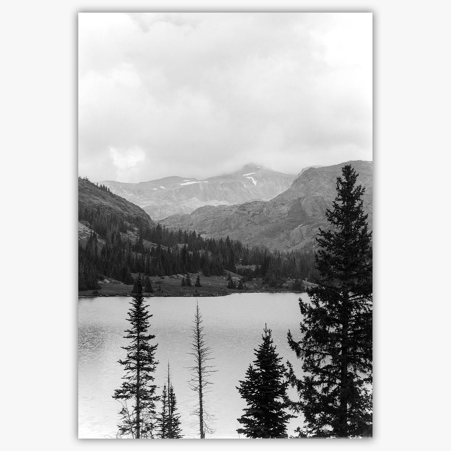 A lake is surrounded by a forest and mountains under a cloudy sky.
