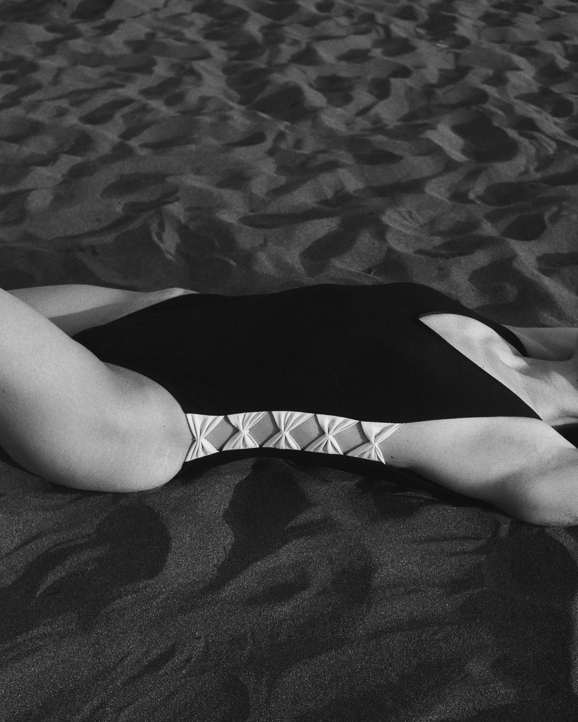 A woman in a swimsuit is lying on a sandy beach.