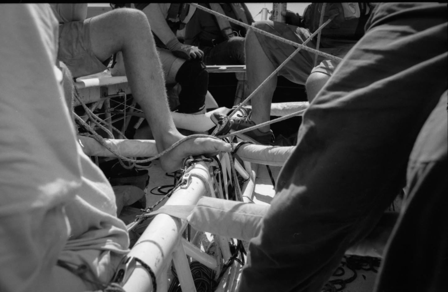 A group of people are sitting on a boat with ropes and equipment around them.