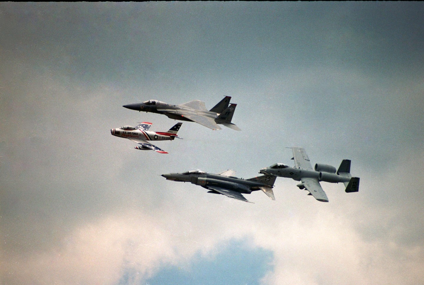 Five military aircraft fly in formation against a cloudy sky.