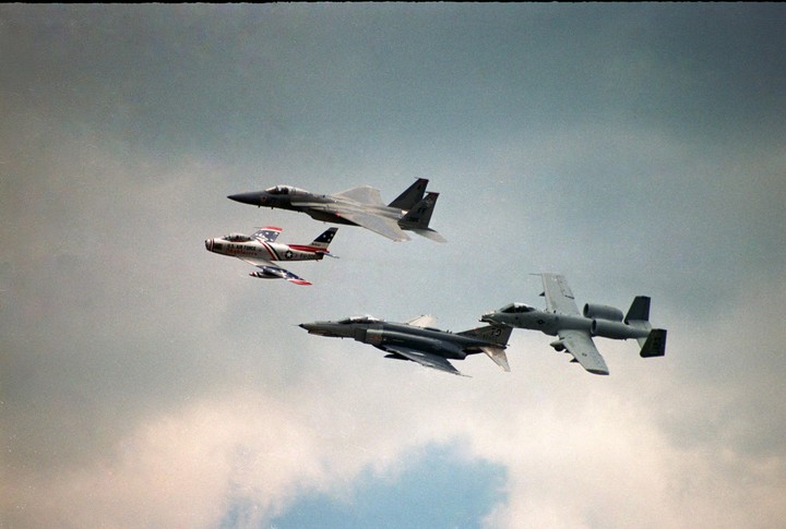 Five military aircraft fly in formation against a cloudy sky.
