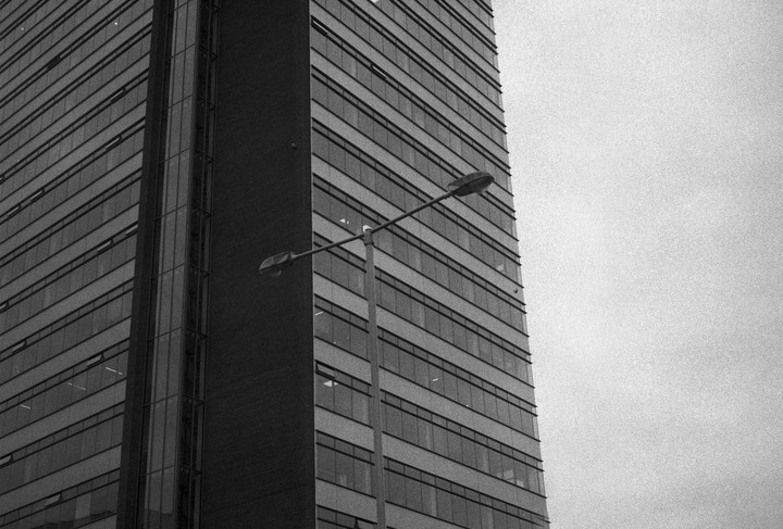 A tall building with many windows stands next to a street light against a plain sky.