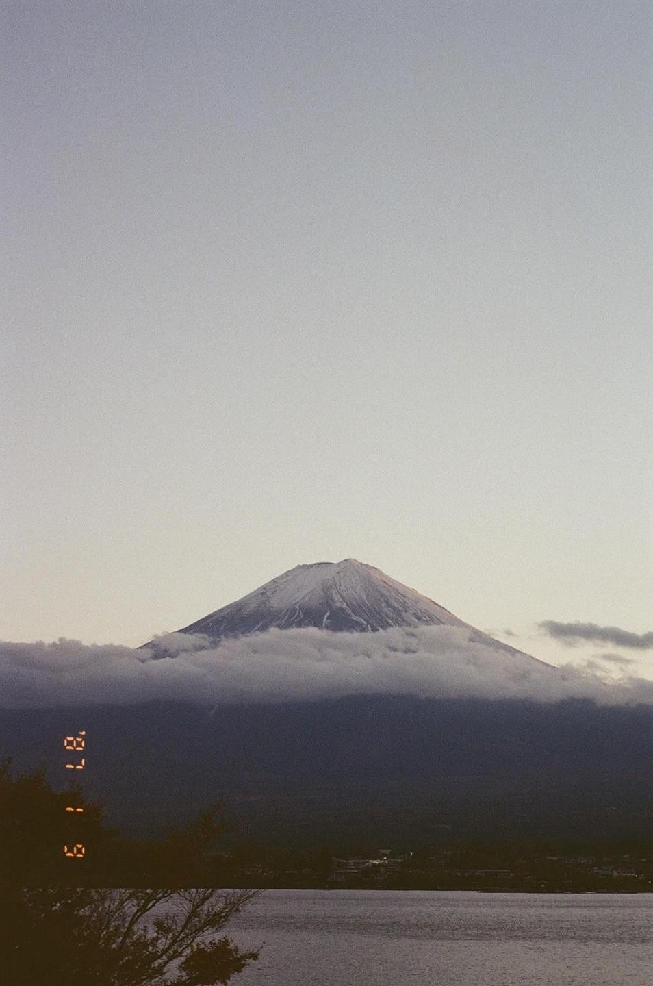 Mount Fuji is visible with its snow-capped peak above a layer of clouds, overlooking a body of water.
