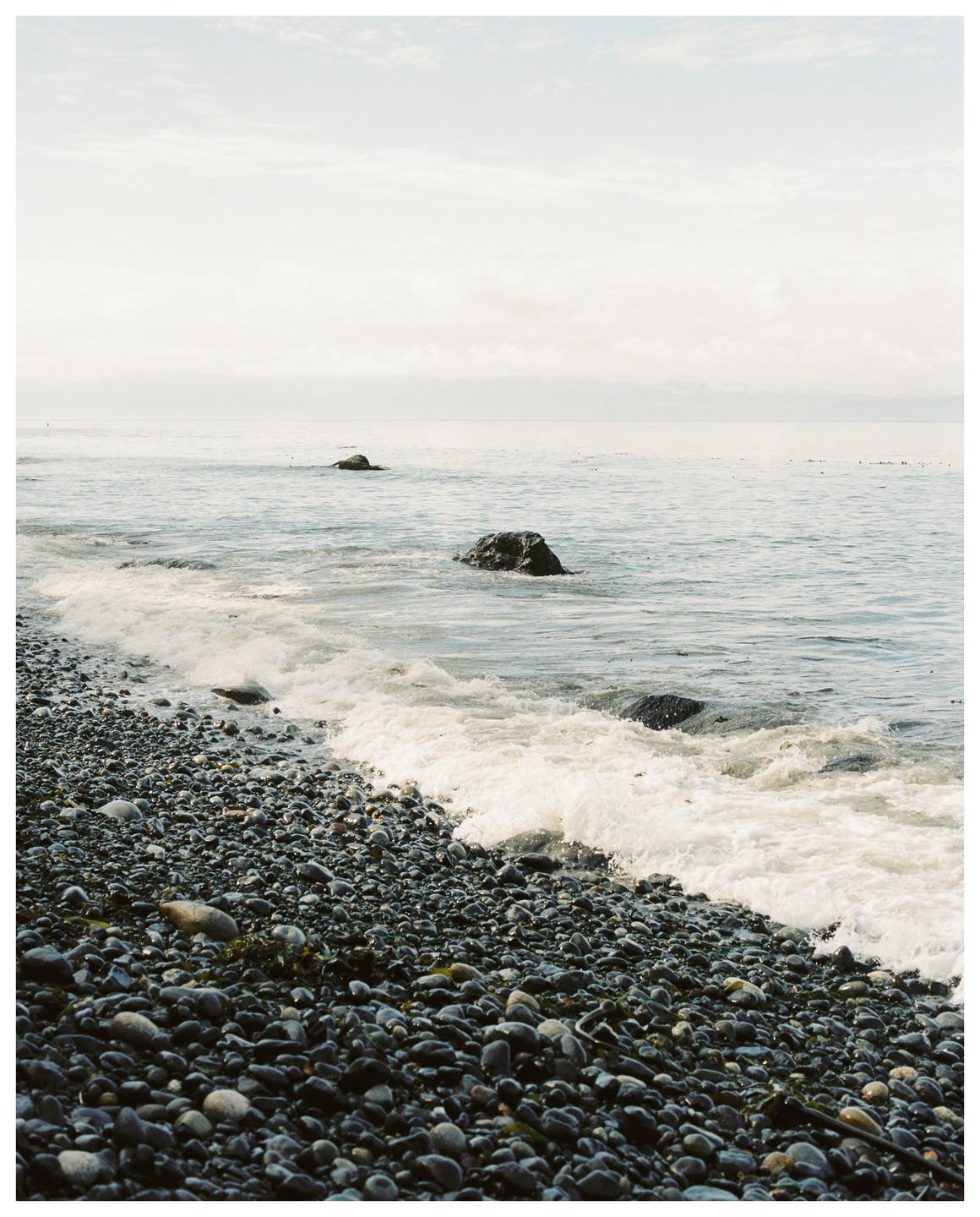 Waves crash on a rocky beach with two large rocks visible in the water.