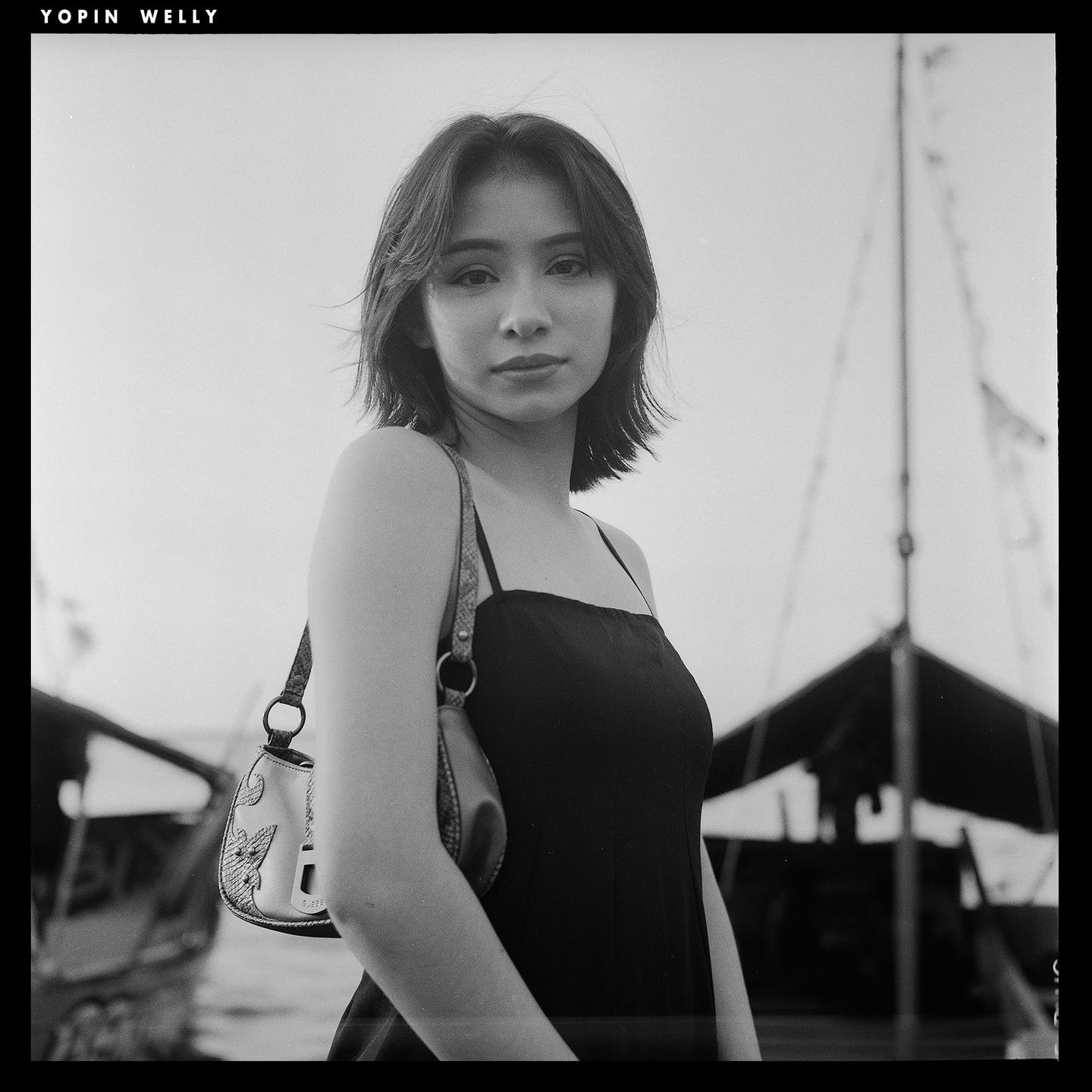 A woman with short hair and a shoulder bag stands in front of boats.