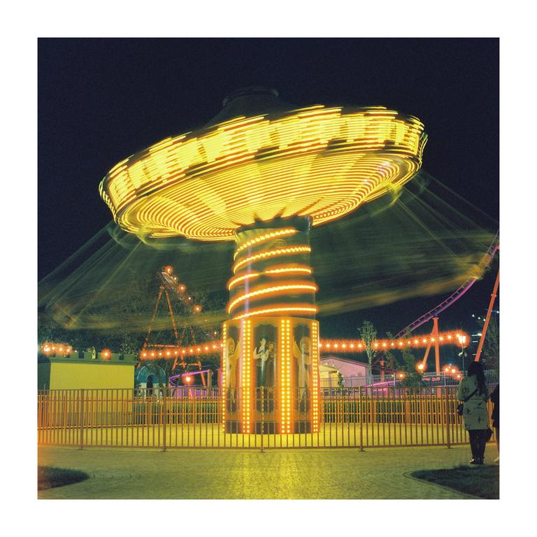 A brightly lit carousel spins at night in an amusement park.
