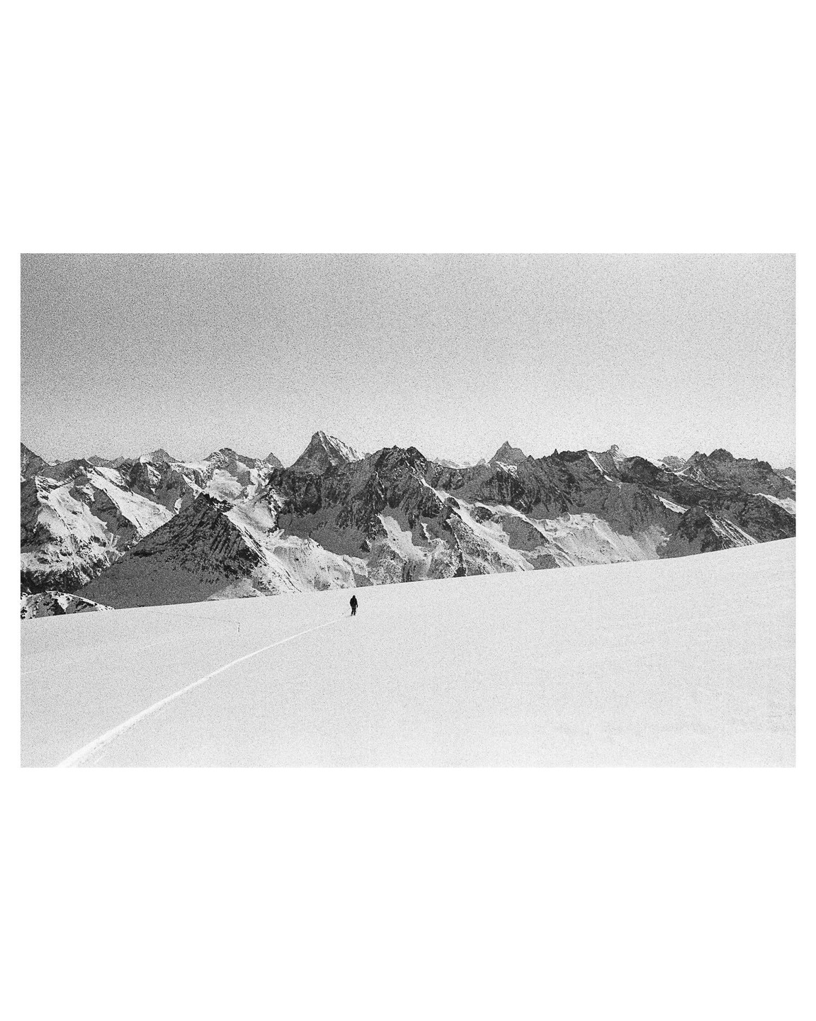 A lone skier is on a vast snowfield with a mountain range in the background.