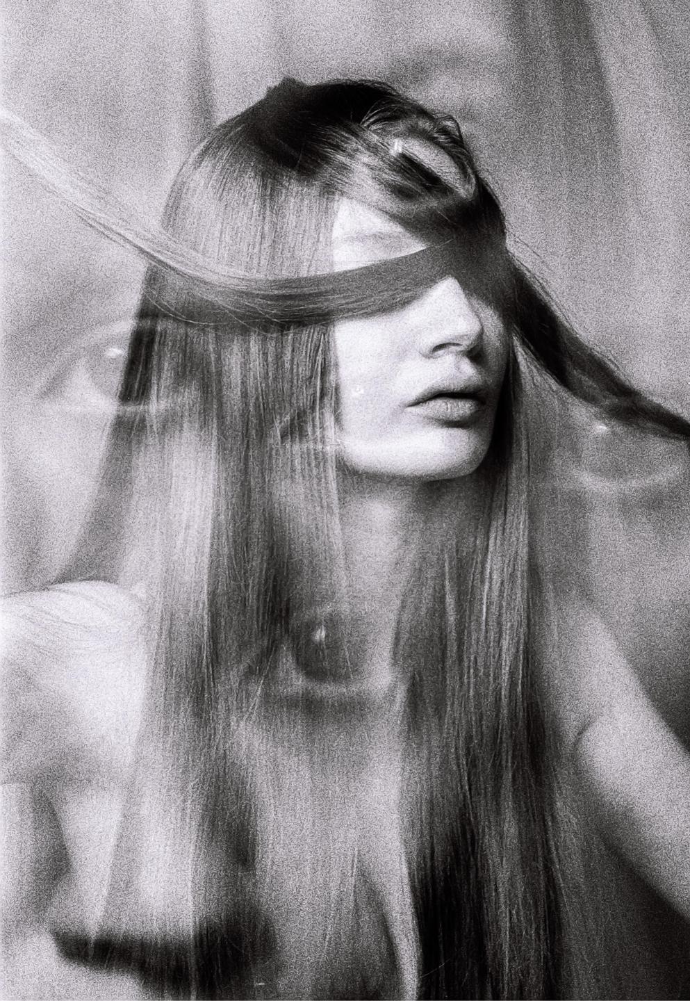 A woman with long hair has a strand of hair covering her eyes in a black and white portrait.