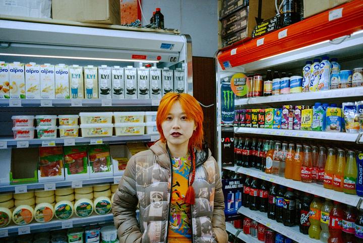 A woman with orange hair stands in a grocery store aisle.