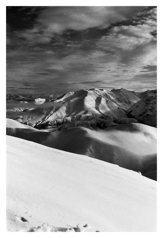 A black and white landscape shows snow-covered mountains under a cloudy sky.