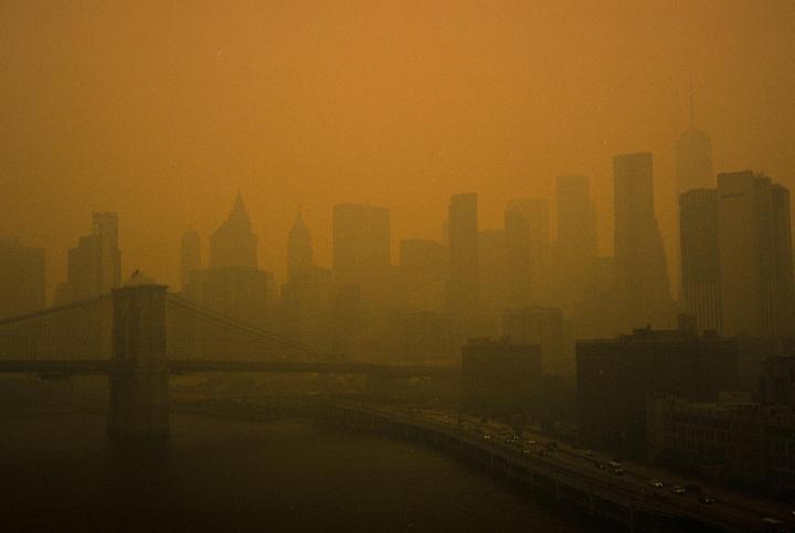 A hazy, orange-tinted skyline of a city with a bridge and a highway over water is visible.