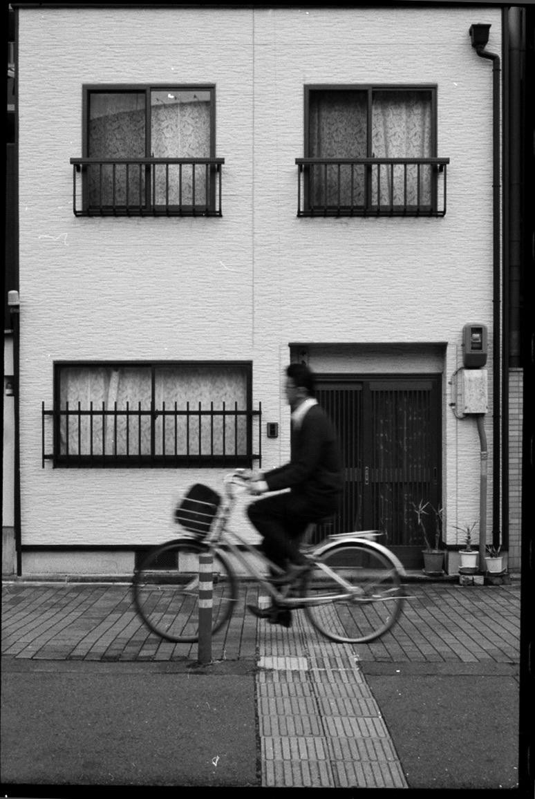 A man rides a bicycle past a building with balconies and windows.