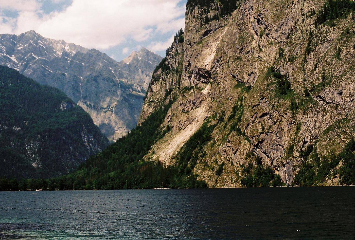 A large body of water is in the foreground with mountains and trees in the background.