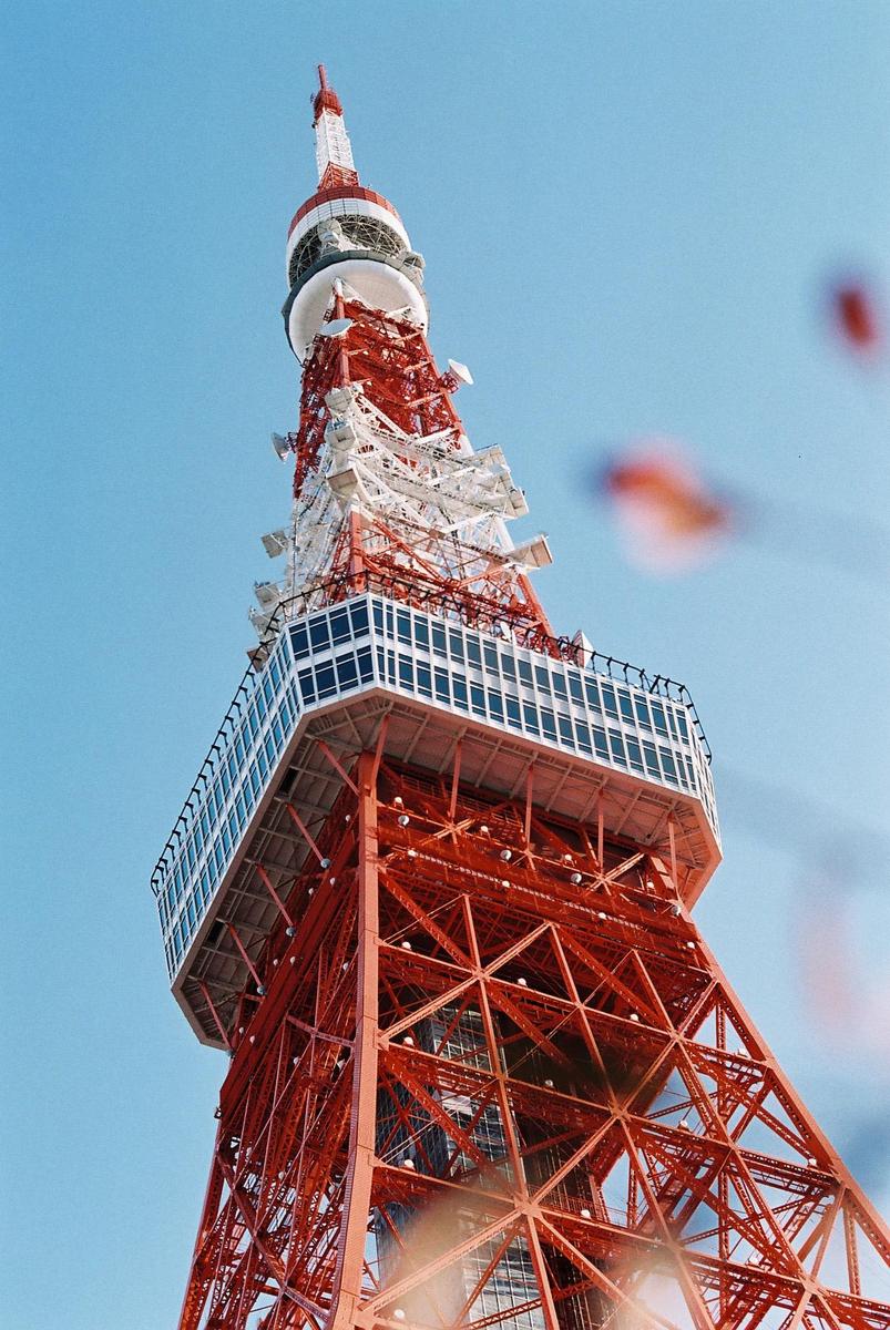 The Tokyo Tower stands tall against a clear blue sky, with its red and white structure visible from a low angle.