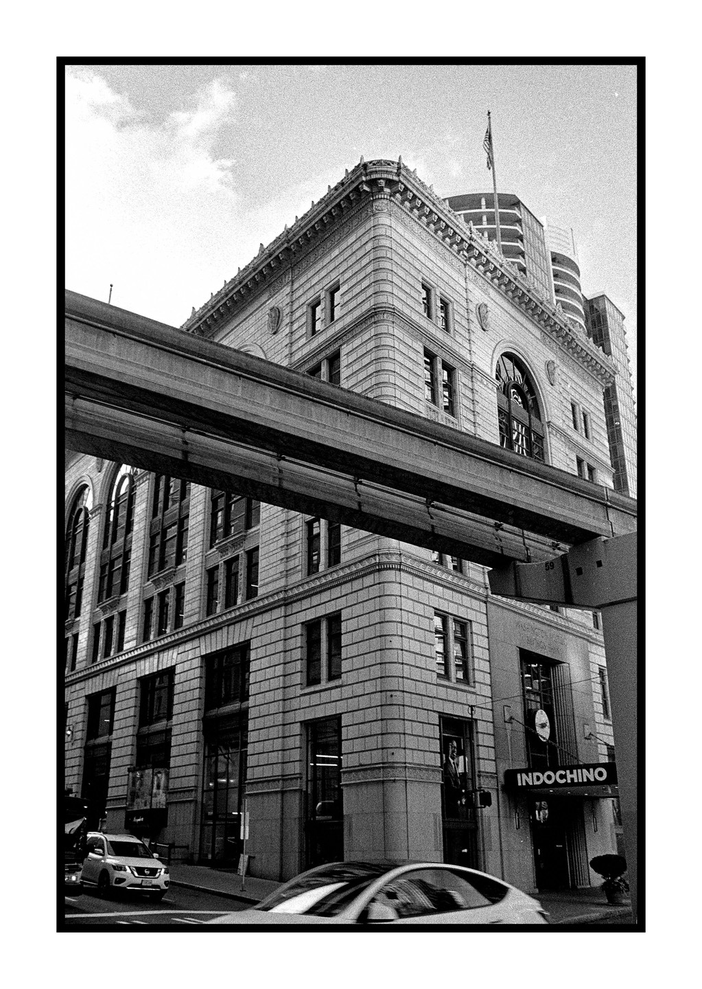 A monorail track crosses in front of a large, ornate building with an "INDOCHINO" sign on the street level, with cars visible below.