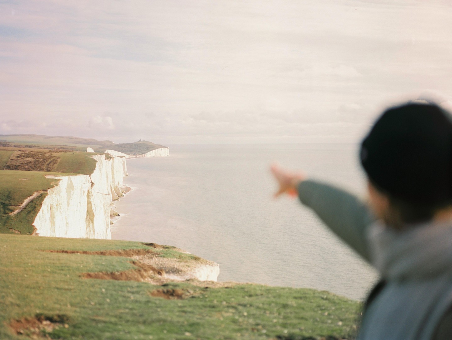 A person points towards a long line of white cliffs along a coastline.
