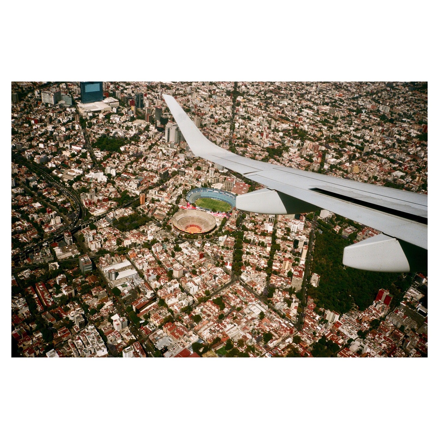 An airplane wing is visible over a sprawling city with two stadiums.