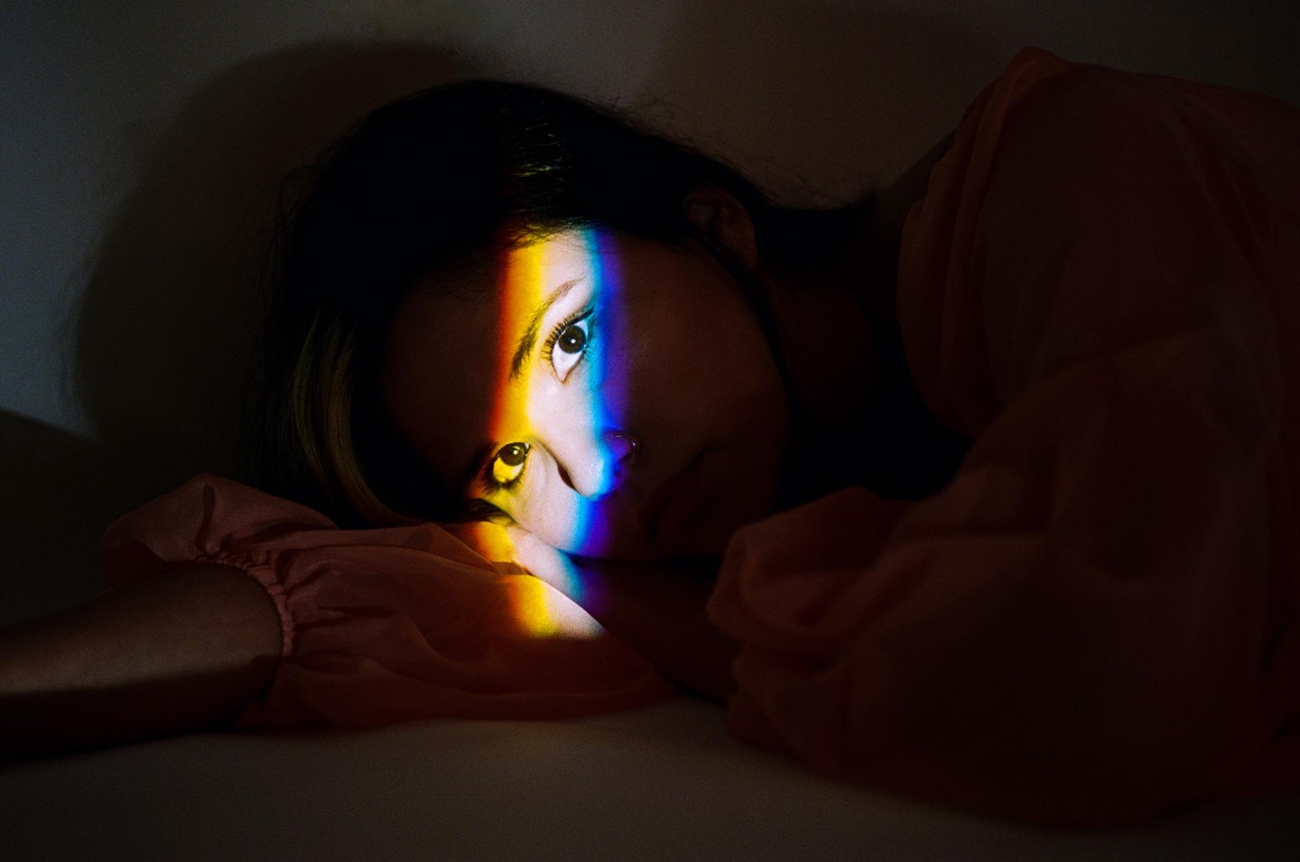 A woman lies down with a rainbow light across her face.