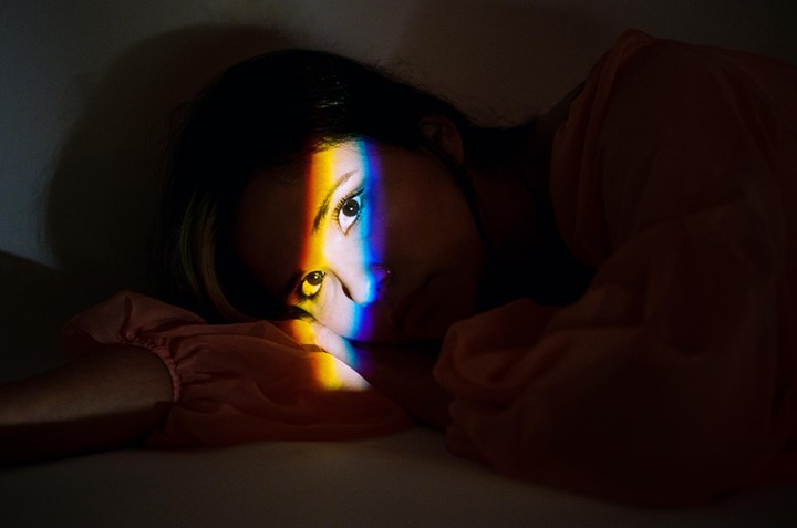 A woman lies down with a rainbow light across her face.