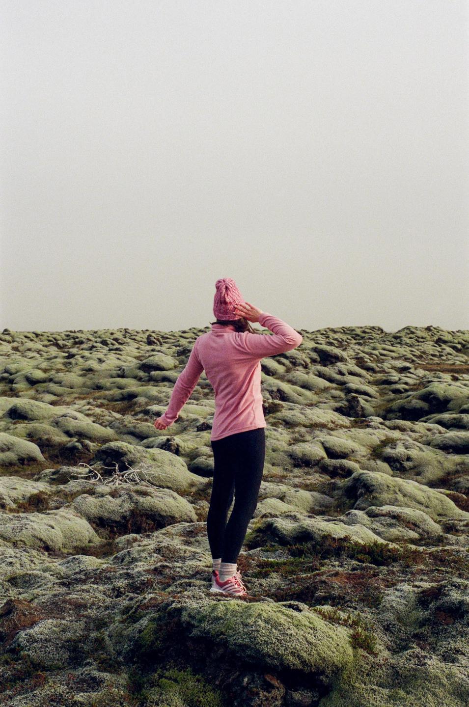 A woman in a pink hat and shirt stands on a mossy landscape under a pale sky.