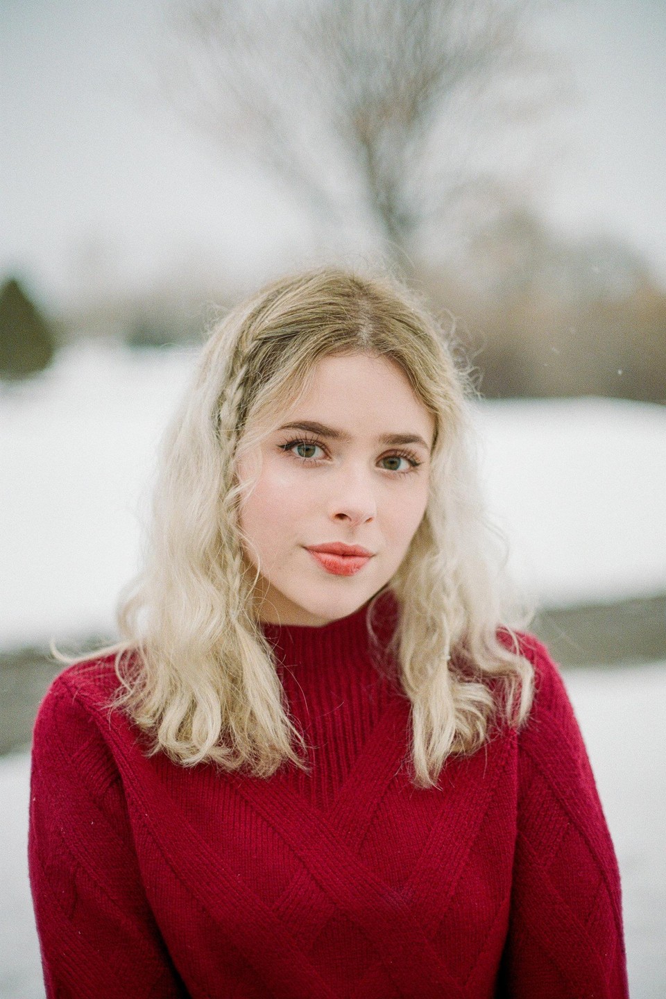 A woman with blonde hair and a red sweater stands in a snowy landscape.