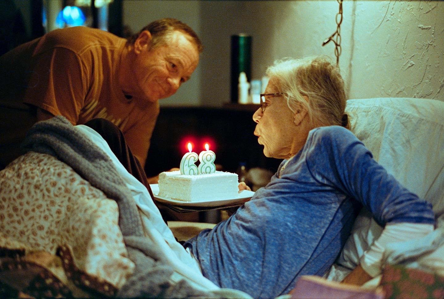 A man watches a woman blowing out candles on a birthday cake.
