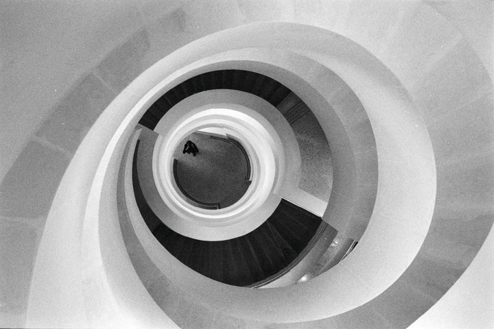 A person stands at the bottom of a spiral staircase in a modern building.