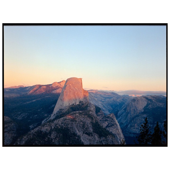A mountain range with a prominent peak is illuminated by the setting sun under a clear sky.