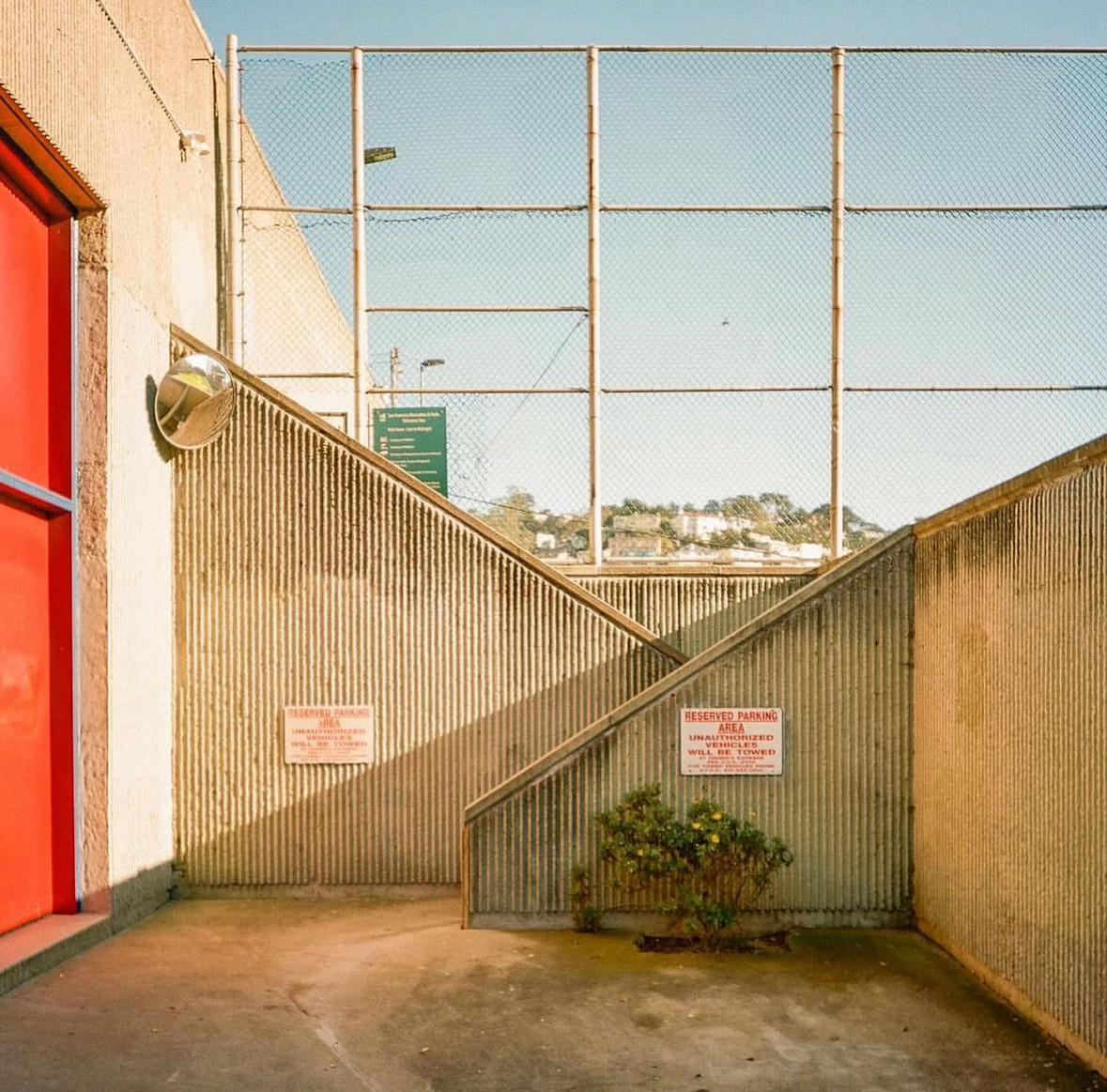 A concrete stairwell with a red door and a chain-link fence is visible under a clear sky.