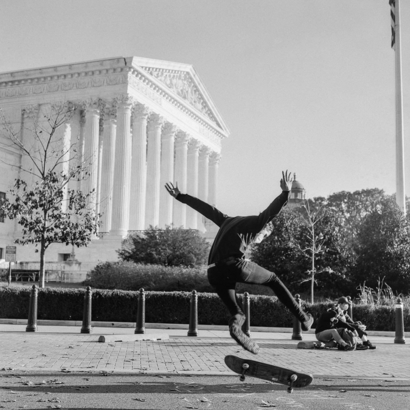A person is captured mid-air on a skateboard in front of a large building with columns.